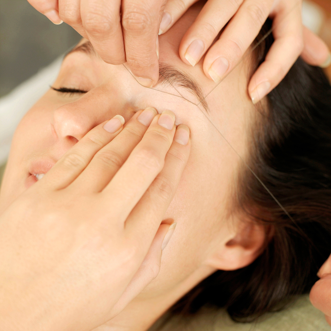 hand using thread to remove facial hair from woman's face